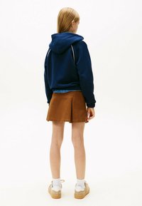 Granatowy hoodie ze sznurkiem i białymi detalami, połączony z brązową spódnicą plisowaną. Modelka nosi białe skarpetki i beżowe sneakersy.