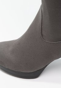 Gros plan d'une bottine en daim gris à bout pointu et talon compensé noir bas.