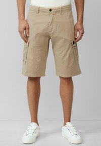 Shorts cargo beiges avec une coupe décontractée, en tissu léger. Dotés de poches appliquées, de passants de ceinture et d'ourlets roulés. Associés à des baskets blanches.