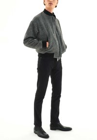 Chaqueta bomber a cuadros grises con cuello, suéter negro debajo, pantalones negros ajustados y botas Chelsea negras.