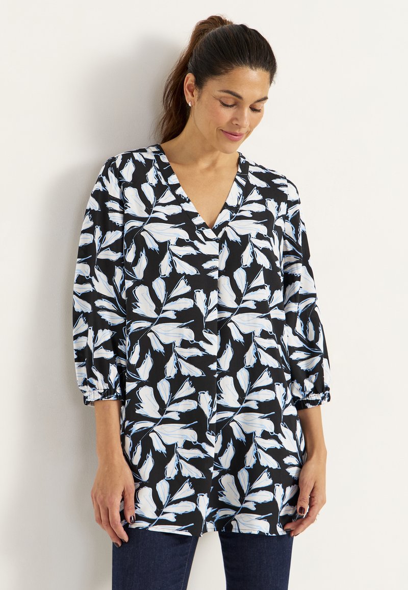 Zwarte blouse met een wit en lichtblauw bloemenpatroon, V-hals en driekwart mouwen met elastische manchetten. Zachte stofafwerking.