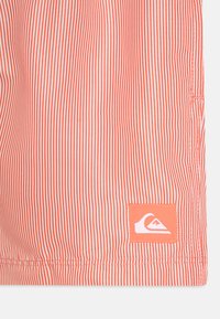 Tkanina crveno-bijelih pruga s glatkom teksturom; na donjem desnom kutu se nalazi zakrpa s logom Quiksilver.