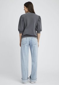 Haut gris à manches bouffantes avec un col rond associé à un jean taille haute bleu clair, offrant une coupe décontractée et des poignets retroussés.