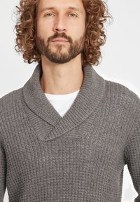 Grauer Strickpullover mit Schalkragen, gerippter Textur und lockerer Passform, über einem weißen Hemd getragen.