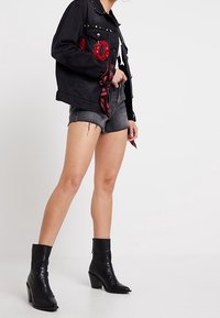 Czarna kurtka dżinsowa z srebrnymi ćwiekami, czerwonym detalem i bandaną. Do tego szare szorty i czarne botki na obcasie do kostki.