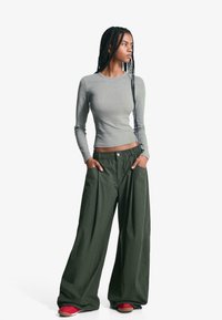 Top gri cu mâneci lungi, strâmt, combinat cu pantaloni verzi largi, comozi, cu talie elastică și buzunare, purtați cu pantofi roșii.