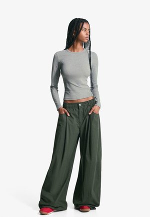 Top gri cu mâneci lungi, strâmt, combinat cu pantaloni verzi largi, comozi, cu talie elastică și buzunare, purtați cu pantofi roșii.