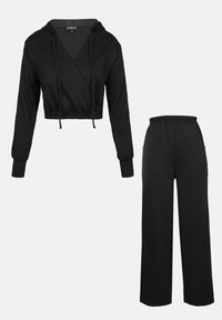 Sudadera negra corta con cordones y mangas largas combinada con pantalones negros de corte holgado que cuentan con una cinturilla elástica y bolsillos laterales.
