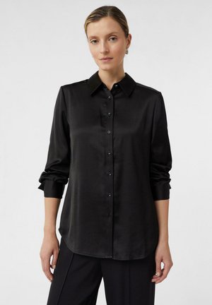 Black satin button-up shirt with a collar, long sleeves, and rolled cuffs. Smooth texture and a curved hemline. Subtle sheen.