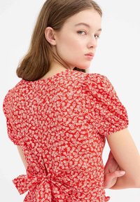 Vestido rojo con un patrón floral, mangas abullonadas y detalle de lazo en la parte posterior, hecho de una tela ligera con un acabado texturizado.