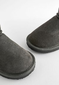 Grå mocka ankelskor med rund tå, sömdekorerad, och gummisula, med en slät textur och minimala designinslag.