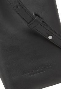 Czarna skórzana torba o gładkiej fakturze, z długim paskiem i wytłoczonym logo marki. Widoczne elementy do regulacji na pasku.