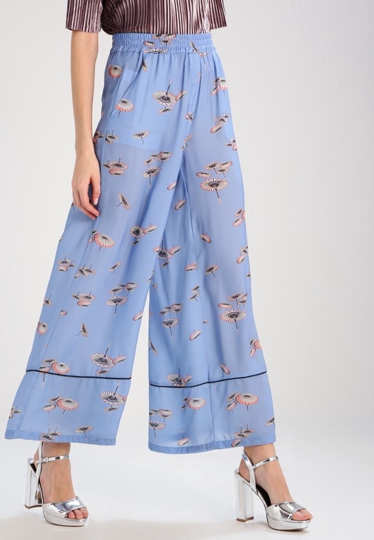 Pantalon bleu à jambes larges avec imprimé parapluie fleuri, taille élastique et sandales ouvertes à talons hauts argentées portées par un mannequin.