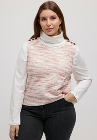Czerwono-biała, paskowana, dzianinowa bluzka bez rękawów z wysokim kołnierzem, z brązowymi guzikami na ramieniu, zestawiona z białą koszulą z długim rękawem.