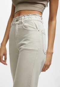 Pantalon beige taille haute avec ceinture élastique, doté de poches latérales et d'une coupe droite. Matière en coton doux texturé.