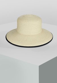 Breiter Strohhut in hellbeige mit strukturiertem Gewebe und einem kontrastierenden schwarzen Rand am Rand. Rundes Kronendesign.