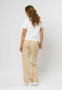 Hvid kortærmet t-shirt parret med beige brede bukser, der har en glat tekstur og en afslappet pasform, båret med hvide sneakers.