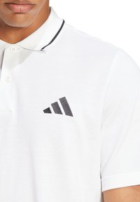 Weißes Polohemd aus strukturiertem Stoff, mit einem schwarzen, auf der Brust gestickten Drei-Streifen-Logo und einem schwarz akzentuierten Kragen.