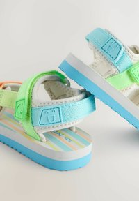 Laste värvilised sandaalid siniste talladega, triibulised jalatoed ja reguleeritavad sinised ja rohelised rihmad, millel on naerunäo ikoonid.