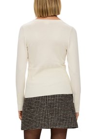 Pull ajusté crème clair à manches longues avec ourlets côtelés, associé à une jupe pied-de-poule noire et blanche. Texture lisse.