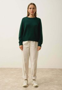 Zielony sweter z dzianiny o okrągłym dekolcie i długich rękawach, w zestawie z jasnobeżowymi spodniami o ciekawej fakturze i beżowymi butami sportowymi.