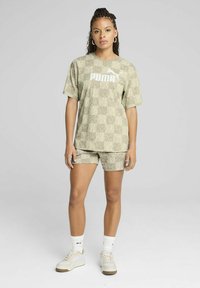 Licht olijfgroen sportset met een gestreepte T-shirt met korte mouwen en shorts, voorzien van een wit Puma-logo. Gecombineerd met witte sneakers.