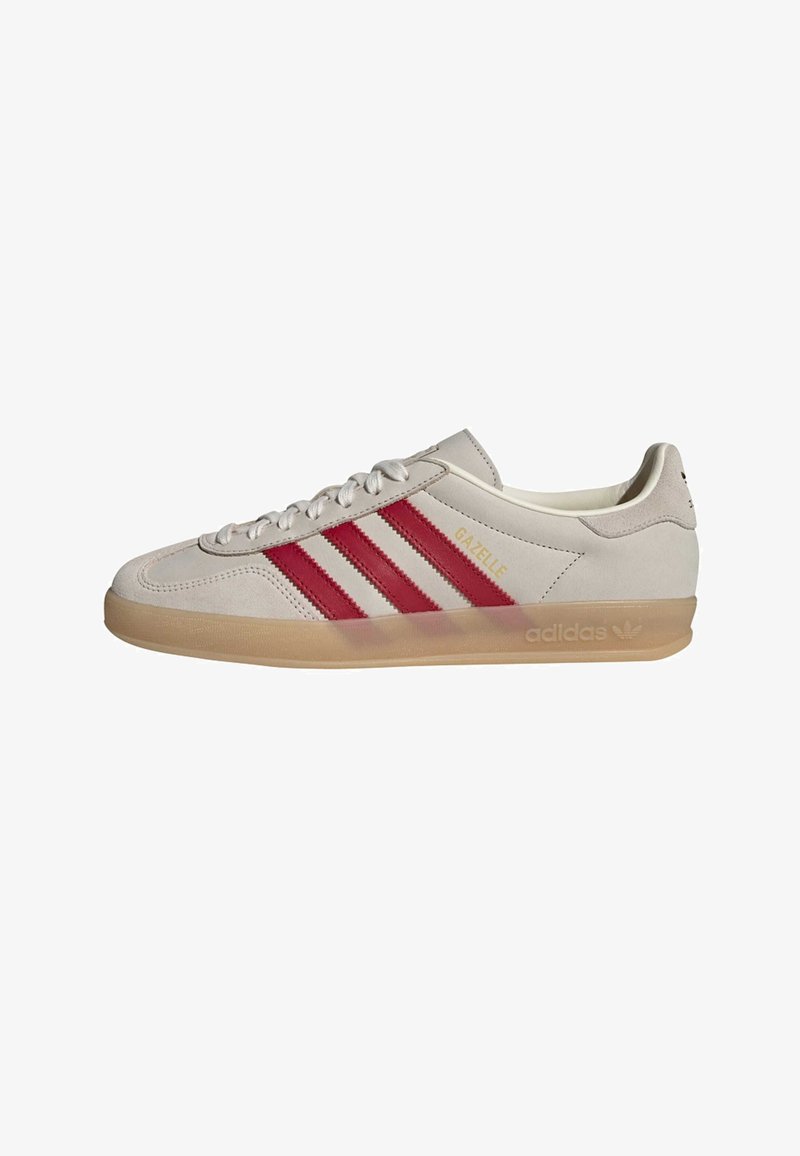 Αθλητικά παπούτσια Adidas Gazelle από σουέντ εκρού με κόκκινες δερμάτινες ρίγες, ελαφρώς καφέ καουτσούκ σόλα και χρυσές λεπτομέρειες με λογότυπο στο πλάι.