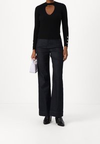 Haut noir côtelé à manches longues avec un col en trou de serrure, associé à un pantalon large en denim foncé, avec un détail de bouton sur les manches.