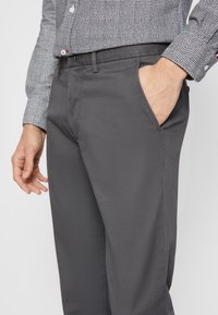 Šedé kalhoty s hladkým povrchem, vybavené bočními kapsami a přiléhavým střihem, spárované s vzorovanou černobílou košilí.