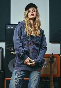 Felpa navy con stampa grafica raffigurante un cuore spezzato, abbinata a jeans blu scoloriti decorati con intricati disegni e ricami.