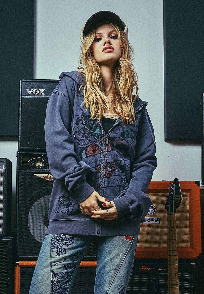 Felpa navy con stampa grafica raffigurante un cuore spezzato, abbinata a jeans blu scoloriti decorati con intricati disegni e ricami.