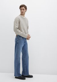 Striped beige long-sleeve shirt with navy and brown stripes, paired with light blue wide-leg jeans. Black shoes complete the outfit.