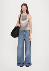 Stripet tanktopp i brun og hvit, kombinert med vide blå jeans. Modellen holder en teksturert svart vevd veske. Flate sko fullfører antrekket.