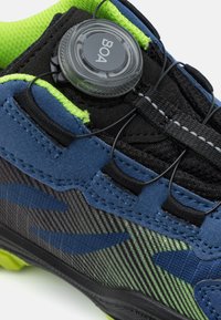 Scarpa sportiva blu e nera con tessuto strutturato, sistema di allacciatura BOA, accenti verdi e un motivo a strisce sulla parte esterna inferiore.