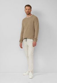 Beige Rippenpullover, cremefarbene Cargo-Hose, weiße Sneaker; verfügt über einen Rundhalsausschnitt und einen Kordelzug in der Taille. Minimalistisches Design und Textur.
