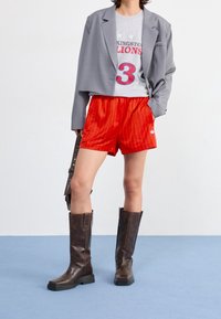 Grå kort kavaj, grå t-shirt med röd text, rödrandiga shorts och bruna knähöga stövlar med tjock klack.