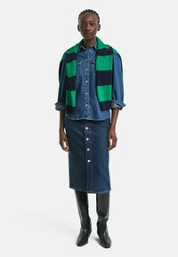 Denim shirt gelaagd met een groen en marineblauw gestreept sweater, gecombineerd met een lange denim rok met knopen aan de voorkant en kniehoge zwarte laarzen.