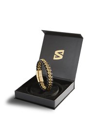 Schwarzes und goldenes Armband mit verflochtenen Gliedern, präsentiert in einer schwarzen Box mit einem weichen, runden Einsatz und einem markierten Logo auf dem Deckel.