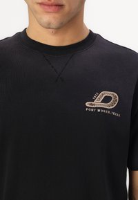 Black cotton t-shirt featuring a round neckline, minimal stitching, and an embroidered logo with "FORT WORTH, TEXAS" in tan.