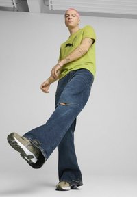Camiseta verde lima con un gráfico de cuadrícula, combinada con pantalones vaqueros de pierna ancha en azul claro con detalles desgastados y zapatillas grises.
