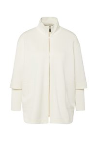 Veste blanche à fermeture éclair avec col montant et manches courtes superposées sur manches longues, dotée de poches avant et d'une fermeture éclair dorée.