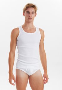 Hvid bomulds tanktop med brede stropper og tætsiddende pasform, parret med hvide, tætsiddende trusser. Glat tekstur, enkelt design.