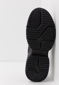 Semelle de basket noire en caoutchouc texturé, présentant un motif géométrique et un marquage. Conçue pour assurer une adhérence sur des surfaces de différentes formes.