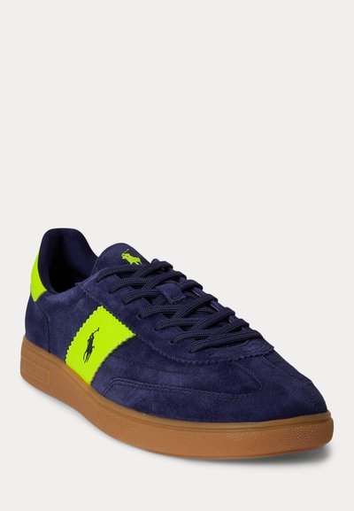 Ναυτικό μπλε σουέντ αθλητικό παπούτσι με λωρίδα λογότυπου σε νέον κίτρινο, ταιριαστές λεπτομέρειες στη φτέρνα και τη γλώσσα, ναυτικά κορδόνια και σόλα από καουτσούκ σε καραμέλα.