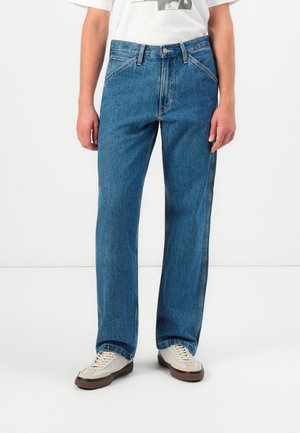 Person wearing straight-cut blue denim jeans with a high waist, paired with white sneakers and a white graphic t-shirt.