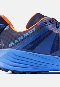 Zilā pārgājienu kurpe ar strukturētu sieta augšdaļu, spilgti oranžiem akcentiem un GORE-TEX zīmolu. Iezīmēta ar rievotu zoli, kas nodrošina saķeri.