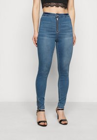 Pantalones vaqueros ajustados de mezclilla azul con cintura alta, cremallera frontal y detalles de cremallera en los puños. Textura suave con un ligero desgaste.