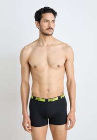 Boxerii negri, cu un logo Puma galben pe talie, design ajustat, realizați dintr-un material neted și elastic, purtați de un model.