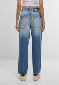 Platas kājas zili džinsi, izgatavoti no denima, ar izbalējušu ombre efektu, izteiktām aizmugurējām kabatām ar šuvju detaļām un melnu logotipa uzlīmi.