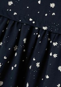 Tela azul marino con estampado floral blanco; presenta un diseño fruncido a lo largo de la costura, una textura suave y patrones de pétalos dispersos.